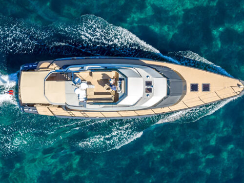 Aerial view of a luxury motor yacht cruising through turquoise sea with a foamy wake behind it.