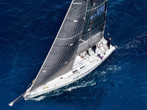 Top-down view of a white sailing yacht cutting through deep blue sea with sails raised on a bright day.