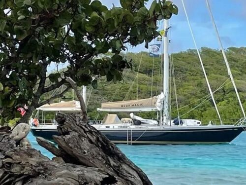 Sailboat named Blue Magic moored beside a rocky mangrove and turquoise water in a tropical bay.