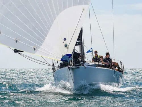 Sailboat cutting through blue sea with white sails and crew aboard on the deck.